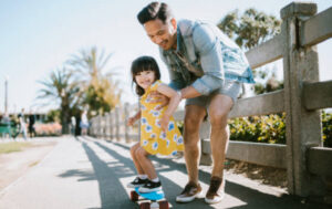 Father Helps Young Daughter Ride Skateboard